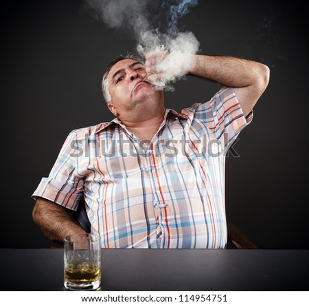 Portrait of a mature mafia man drinking and smoking while sitting at table on gray background