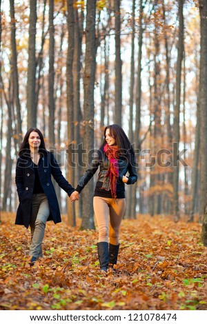Full length portrait of two happy girlfriends walking in the woods while holding hands