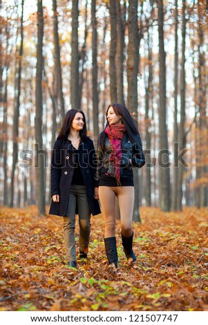 Full length portrait of two happy girlfriends walking in the woods while holding hands