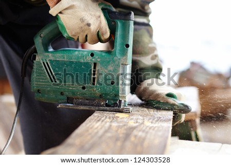 Man with protection gloves using an electric saw to cut a plank