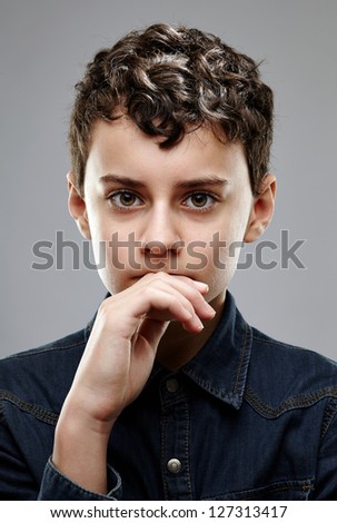 Big brown eyed boy sharing a deep thoughtful expression looking straight at camera, isolated on gray background