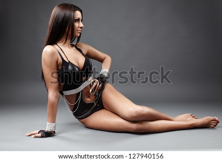 Full length profile of hot exotic dancer in leather lingerie sitting on the floor. One hand in waist.