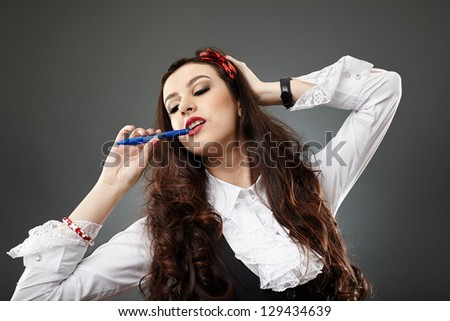 Pretty young woman holding a pen in her mouth, expressing sensuality, over gray background