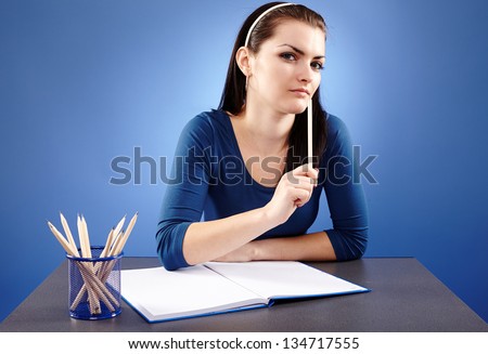 Closeup pose of a pensive young student, sitting at her desktop, on blue background