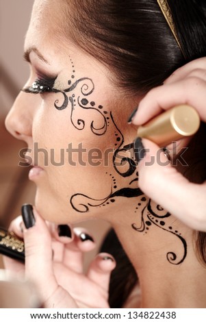 Closeup of a brunette having applied face tattoo by makeup artist