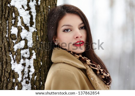 Portrait of a beautiful woman leaning on a tree trunk in the winter
