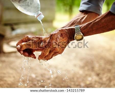 Old man washing his hands with water pouring from a plastic bottle