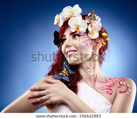 Beautiful redhead young woman with orchids in her hair and fantasy creative makeup over blue background