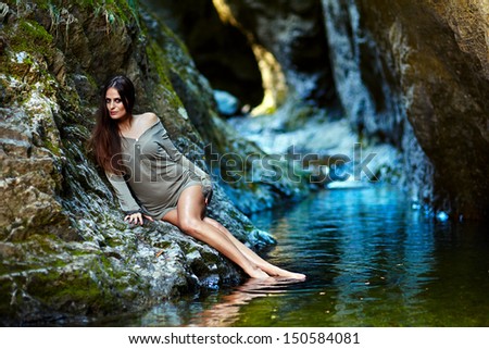 Portrait of a young sexy woman laying on the mountain rock close to a mountain waterfall
