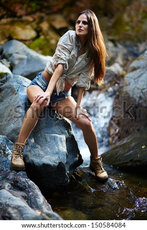 Beautiful young woman leaning on the rocks in the mountains and resting close to a mountain spring
