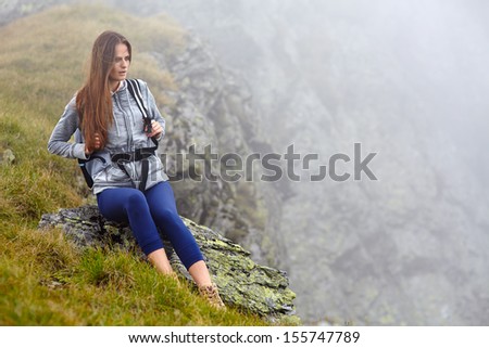 Woman hiker with backpack resting on a rock with a misty background