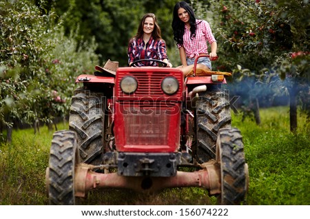 Two attractive female farmers driving the tractor in the orchard