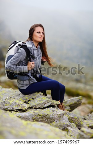 Woman hiker with backpack resting on the mountain rocks