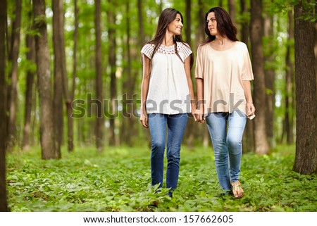Mother and daughter walking hand in hand through a forest and talking