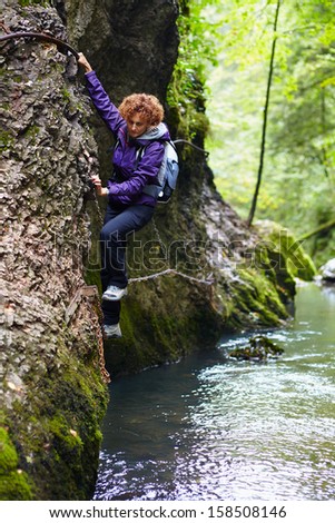 Woman climbing on a mountain wall over a river in a canyon