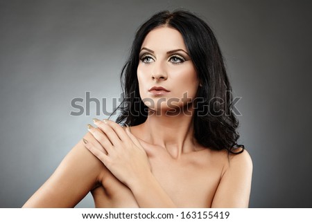 Closeup of beautiful sensual brunette with hand resting on shoulder over gray background