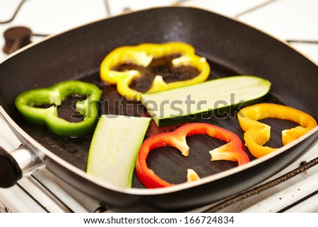 Closeup of fresh slices of zucchini and red, green and yellow pepper in the frying pan on the stove