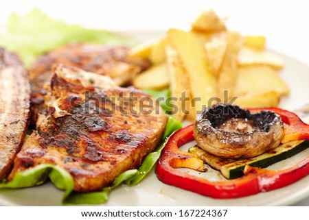 Closeup of pork meat steak, wedges potatoes and vegetables on a plate, isolated on white background. Selective focus