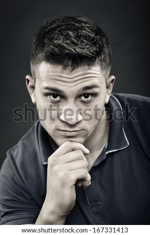 Monochrome portrait of handsome young man wearing a navy blue polo t-shirt with hand on chin