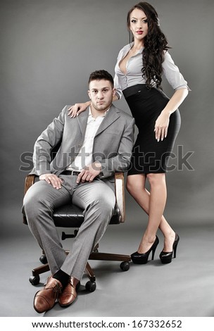 Studio shot of sexy secretary standing near the boss sitting on a chair