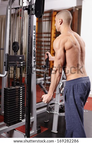 Athletic man working his triceps, pulling heavy weights at the gym