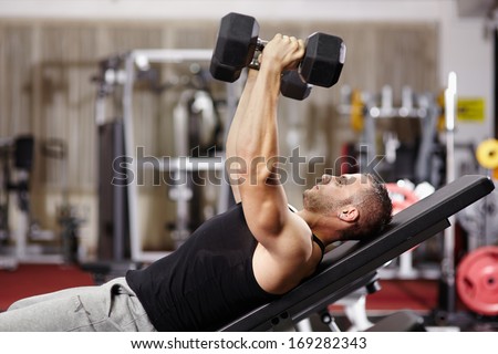 Athletic young man laid on back working his chest with heavy dumbbells
