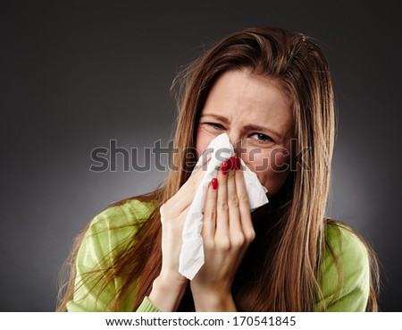 Young woman with bad cold blowing her nose in a white tissue