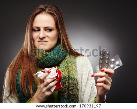 Studio shot of a woman holding a cup of hot tea and expressing disgust to some blister packed tablets she is holding over gray background
