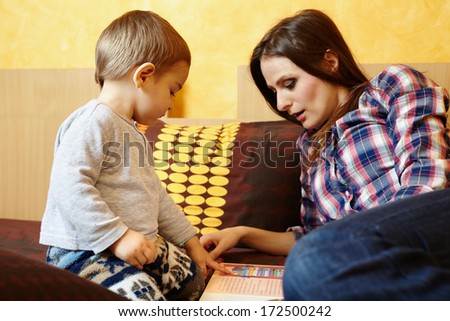 Mother and son reading on a colored book, sitting on bed