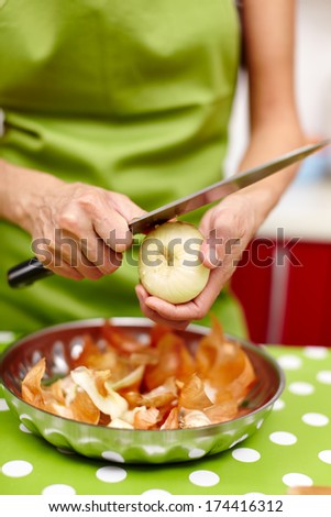 Closeup of the hands of a young woman peeling and cutting onion in the kitchen