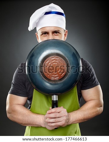 Studio shot of a man chef hiding his face behind a wok pan over gray background