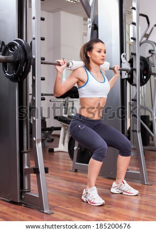 Young athletic woman doing squats with the barbell at the gym