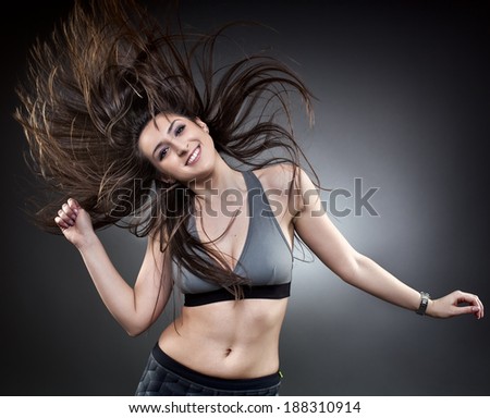 Young woman dancing with her long hair fluttering in motion, studio shot on gray