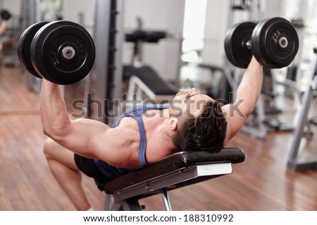 Athletic man working out his chest with dumbbells on a bench press