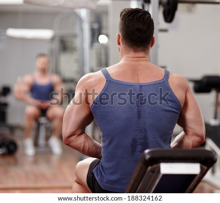 Strong athletic man in gym looking at his reflection in the mirror and preparing for workout