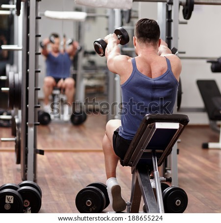 Man doing shoulders and back workout in front of the mirror in the gym