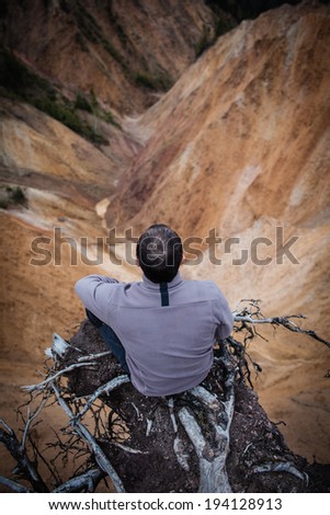 Man sitting on the edge of a high cliff, adrenaline, courage and risk concept