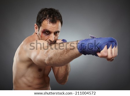 Muay thai or kickbox fighter with bruises and blood on his face, throwing a direct punch
