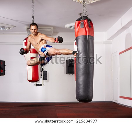 Kickboxer deploying a jump kick on a punchbag in the gym