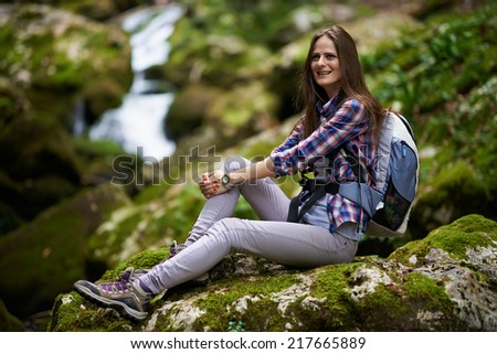 Young woman hiker with backpack resting on moss covered rocks in a canyon