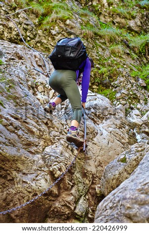 Image from the back of a young woman climbing on the rocks of a steep mountain