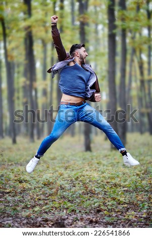 Happy young caucasian man jumping for joy outdoor in a forest