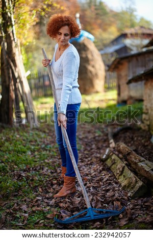 Caucasian farmer woman with a rake cleaning her garden of fallen leaves
