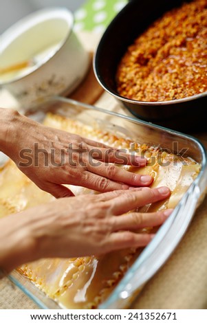 Woman cooking lasagna, arranging the pasta in a tray with filling