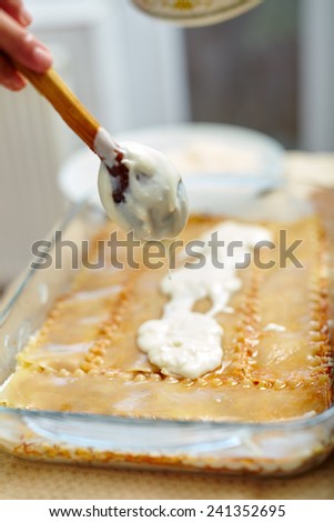 Woman spreading bechamel sauce on lasagna pasta in a tray