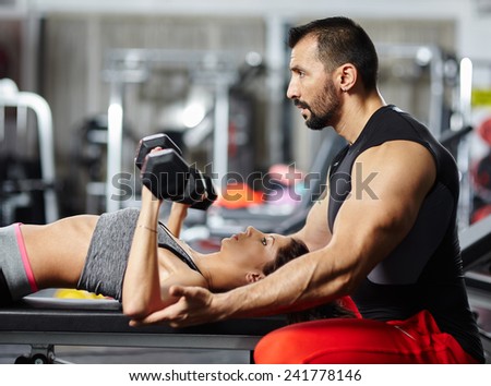 Personal fitness trainer assisting a young woman in the gym at a workout