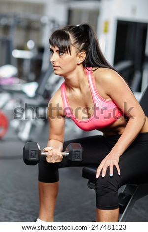 Young woman doing biceps workout with dumbbells in a gym