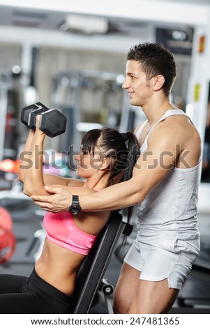 Personal fitness instructor helping a young woman work out with dumbbells