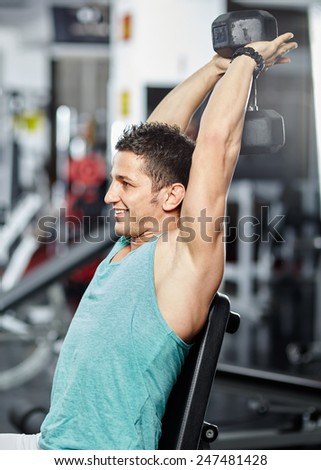 Young athletic man doing triceps and shoulder workout in a gym