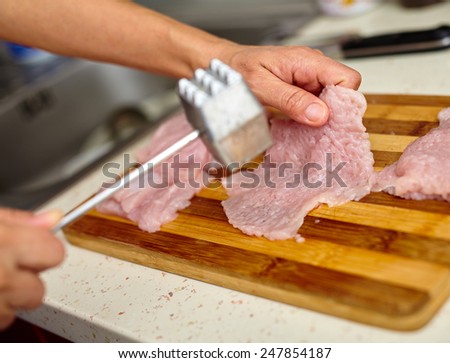 Woman cook beating turkey breast fillets with meat tenderizer